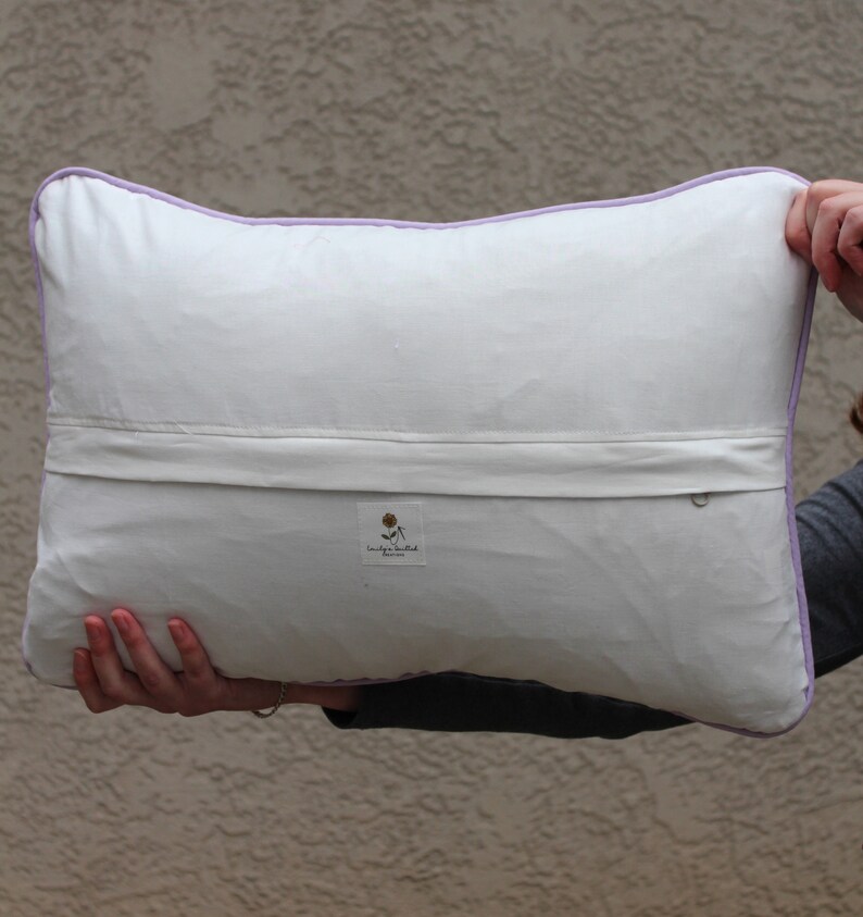 This shows the back of the pillow. The fabric is white, and there is a horizontal flap that runs the whole pillow to cover the zipper. In the center is a tag that states my business name.