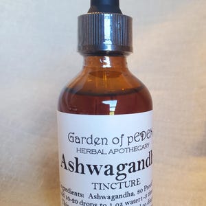 May include: A brown glass bottle with a dropper top and a white label that reads "Garden of pedes HERBAL APOTHECARY Ashwagandha TINCTURE Ingredients: Ashwagandha, 80 Proof 10-20 drops to 1 fl oz water 1-3 times daily. This product is not intended to diagnose, treat, cure, or prevent any disease. Net Wt. 2 fl oz (60 ml)"