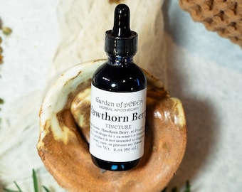 Puede incluir: Una botella de 2 onzas (60 ml) de tintura de bayas de espino blanco de Garden of peDEN Herbal Apothecary. La botella es de vidrio oscuro con una tapa de gotero negro y una etiqueta blanca con texto negro.