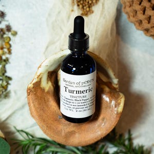 May include: A small glass bottle with a black dropper top, containing a dark liquid. The bottle is labeled "Garden of pеден HERBAL APOTHECARY Turmeric TINCTURE Turmeric, Black Pepper, Pro 20-30 drops to 1 oz water-3 times a day. This product is not intended to diagnose, treat, cure, or prevent any disease. Net Wt. 2 oz (60 mL)"