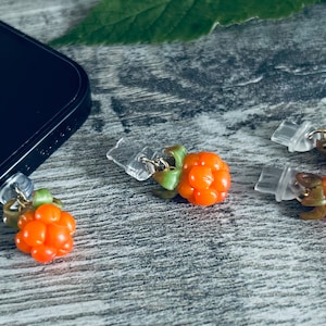 Op de afbeelding: Vier oranje en groene wolkbes-telefooncharms met doorzichtige plastic sluitingen. De charms liggen op een houten oppervlak.