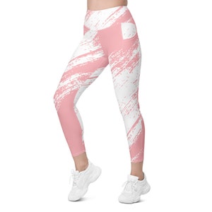 May include: Pink and white leggings with a paint splatter design. The leggings have a high waist and a pocket on the right side.