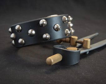May include: A black leather bracelet with silver studs. The bracelet is lying on a black surface.