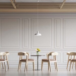 May include: A white, minimalist dining room with four white pendant lights hanging from the ceiling. There are three round tables with four chairs each. The chairs are made of light wood and have a simple design. The tables are made of wood and have a light brown finish. There are small bouquets of yellow flowers on each table.