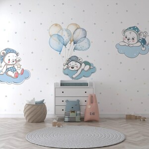 Può includere: Una cassettiera bianca con tre cassetti, un tappeto blu chiaro, un cesto di vimini marrone, un peluche rosa e bianco, un peluche patchwork blu e bianco e una parete bianca con una nuvola blu e bianca con un orso che dorme, una nuvola blu e bianca con un orso che tiene una stella e una nuvola blu e bianca con un orso con un cappello blu e bianco.