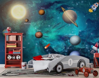 Può includere: Un murale a tema spaziale blu e verde con pianeti, stelle e una cometa. Il murale è in una camera da letto per bambini con una libreria rossa, un letto grigio e un'auto giocattolo rossa.