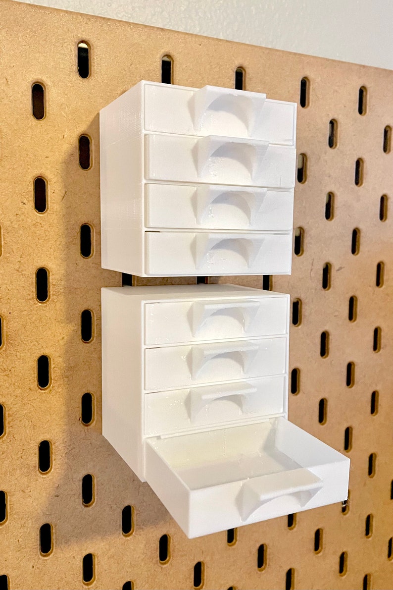 Puede incluir: Organizador de cajones de pl&aacute;stico blanco con seis cajones peque&ntilde;os y un caj&oacute;n m&aacute;s grande. El organizador est&aacute; montado en una pared de tablero de clavijas.