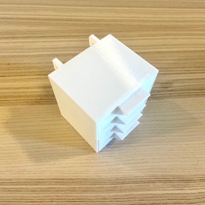 Puede incluir: Cubo de pl&aacute;stico blanco con una serie de peque&ntilde;as aberturas rectangulares inclinadas en un lado.