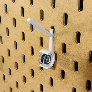 May include: A white pegboard hook with a clear plastic holder, designed to hold items. The hook is attached to a brown pegboard with evenly spaced oval holes. The holder contains a blue object.