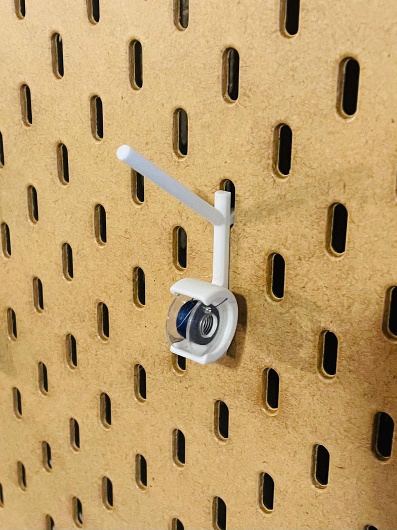 May include: A white pegboard hook with a clear plastic holder, designed to hold items. The hook is attached to a brown pegboard with evenly spaced oval holes. The holder contains a blue object.