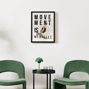 Op de afbeelding: Een ingelijste kunstdruk met de woorden "MOVEMENT IS MEDICINE" en een illustratie van een persoon in een yogahouding. De print zit in een zwart frame en hangt aan een witte muur. Twee groene stoelen en een kleine tafel met een groene lamp staan ervoor.
