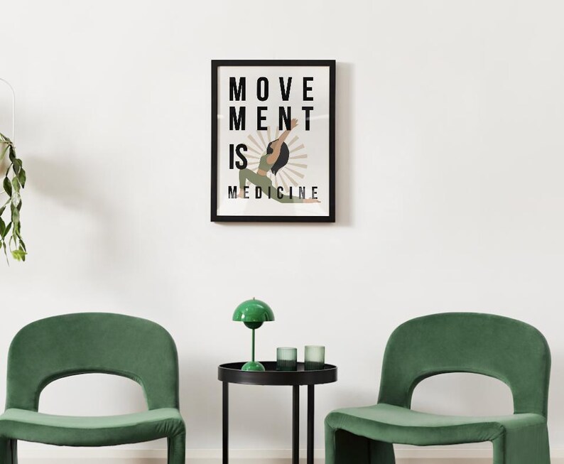 Op de afbeelding: Een ingelijste kunstdruk met de woorden "MOVEMENT IS MEDICINE" en een illustratie van een persoon in een yogahouding. De print zit in een zwart frame en hangt aan een witte muur. Twee groene stoelen en een kleine tafel met een groene lamp staan ervoor.