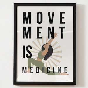 Op de afbeelding: Ingelijste kunstafdruk met de tekst "MOVEMENT IS MEDICINE" in zwarte letters. De afbeelding toont een vrouw in een yogahouding, gekleed in groene sportkleding, met een sunburst-ontwerp erachter. De lijst is zwart.