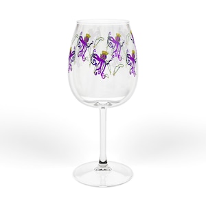 May include: A clear wine glass with a decorative design of purple octopuses wearing gold crowns. The octopus design is repeated around the glass. The glass has a long stem and a round base.