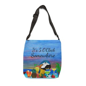 May include: A blue crossbody bag with a black strap. The bag features a tropical scene with a parrot, cocktails, and the text "It's 5 O'Clock Somewhere". The background depicts a sunset over the ocean.