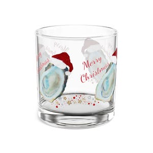 May include: A clear glass tumbler with a festive Christmas design. The tumbler features illustrations of oysters wearing Santa hats, with the words "Merry Christmas" in red script. Gold and red star accents are scattered at the base.