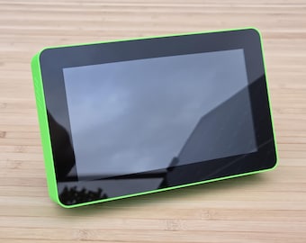 May include: A rectangular tablet with a black screen and a bright green border. The screen reflects the sky and surrounding environment. The device is placed on a light brown wooden surface.