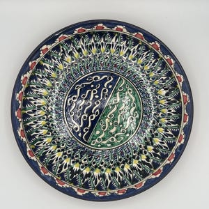 Può includere: Un grande piatto rotondo in ceramica con un design floreale blu, verde e bianco. Il centro del piatto presenta un motivo stilizzato di linee vorticose in blu e verde.