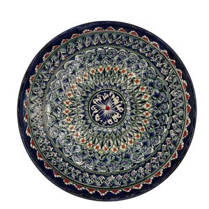 Può includere: Un piatto rotondo in ceramica con un motivo simmetrico dettagliato. Il piatto presenta un bordo blu scuro e un design centrale nei toni del blu, verde e rosso. Gli intricati motivi floreali e geometrici creano un design visivamente accattivante.