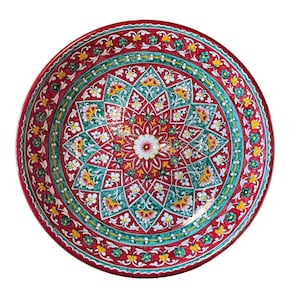 Può includere: Un piatto rotondo e decorativo in ceramica con un vivace motivo floreale. Il piatto presenta uno sfondo rosso con un motivo centrale a forma di mandala in verde acqua, giallo e bianco. Il design intricato include fiori stilizzati e forme geometriche.