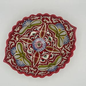 Può includere: Piatto da portata ovale in ceramica dipinto a mano. Il piatto presenta un vivace sfondo rosso con intricati disegni floreali e a volute in blu, verde, bianco e rosso. Il bordo ha un bordo smerlato. Un pezzo decorativo per la casa.