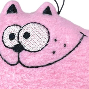 May include: A pink cat-shaped ornament with embroidered black details. The cat has large, expressive eyes, a smiling mouth, and black stripes on its tail. The ornament is made of a soft, fuzzy material.