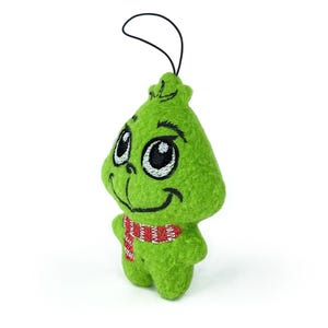 May include: Green plush ornament of the Grinch with a red and white striped scarf. The Grinch has a smiling face with large eyes and a black embroidered nose.