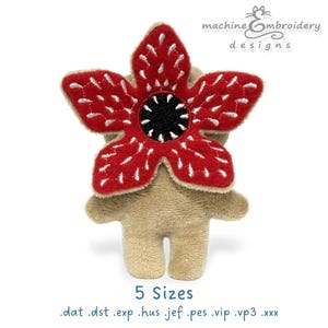Könnte beinhalten: Ein Demogorgon-Plüschtier mit einem roten, blütenblattförmigen Kopf, weißen Nähten und einem schwarzen Zentrum. Der Körper ist beige. Der Text "machine embroidery designs" steht oben. Der Text "5 Sizes" und Dateitypen stehen unten.