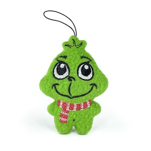 May include: Green plush ornament of the Grinch with a red and white striped scarf. The Grinch has a mischievous grin and large eyes.