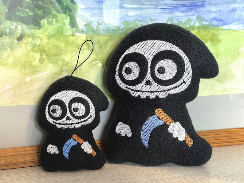 Puede incluir: Dos peluches con forma de parcas de dibujos animados, ambos con t&uacute;nicas negras con capucha, caras de calavera blancas con grandes ojos circulares y una peque&ntilde;a guada&ntilde;a azul claro con mango color canela. El peluche m&aacute;s peque&ntilde;o incluye un lazo negro.