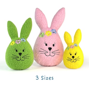 May include: Three Easter bunny decorations in green, pink, and yellow. Each bunny has embroidered facial features and a floral crown. The text "3 Sizes" is below the bunnies.