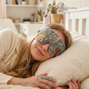May include: A grey sleep mask featuring embroidered illustrations of three cats in yellow, white, and brown. The mask has a contoured shape designed to cover the eyes. Text on the image reads machine embroidery designs, 2 Sizes, .dat .dst .exp .hus .jef .pes .vip .vp3 .xxx.
