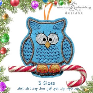 May include: A blue owl Christmas ornament with a candy cane perch. The owl has large eyes, a yellow beak, and brown accents. The ornament is hanging from an orange ribbon. The text "3 Sizes" is below the owl.