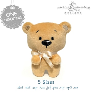 Op de afbeelding: Een zachte, lichtbruine teddybeer met een crème lint om de nek. De beer heeft een zwarte neus en geborduurde details. De afbeelding bevat de tekst "ONE HOOPING" en "5 Sizes". Het logo "machine embroidery designs" is ook zichtbaar.