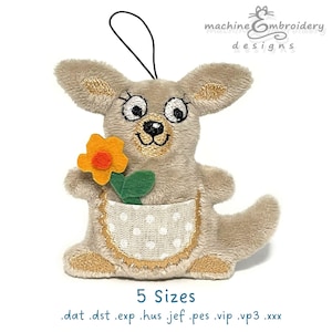 Puede incluir: Adorno de canguro de peluche con detalles bordados, sosteniendo una flor de fieltro. El canguro tiene un bolsillo con un estampado de lunares. El adorno tiene una cuerda negra para colgar. El texto en la imagen dice "machine embroidery designs" y "5 Sizes".