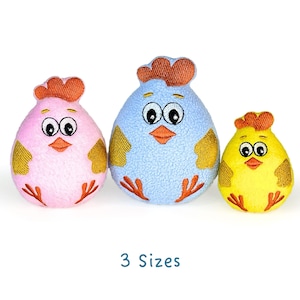 Könnte beinhalten: Drei Plüsch-Kükenspielzeuge in verschiedenen Größen. Das größte Küken ist blau, das mittlere Küken ist rosa und das kleinste Küken ist gelb. Alle drei Küken haben gestickte Augen, Schnäbel und Füße.