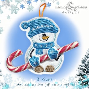 May include: Embroidered snowman ornament with a blue hat, scarf, and mittens, holding a red and white candy cane. The ornament has a smiling face and brown stitched feet. The background includes snowflakes and a blue gradient.