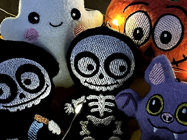 Puede incluir: Una colecci&oacute;n de cinco adornos de fieltro que incluye un fantasma blanco, una calabaza naranja, un esqueleto negro, un murci&eacute;lago morado y una figura negra con rasgos faciales blancos. Cada pieza tiene detalles bordados y peque&ntilde;as luces LED.