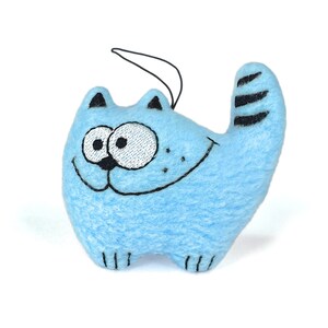 May include: A light blue cat-shaped plush toy with embroidered details. The cat has a smiling face, black whiskers, and a striped tail. It has a black string attached for hanging. The toy is made of soft material.