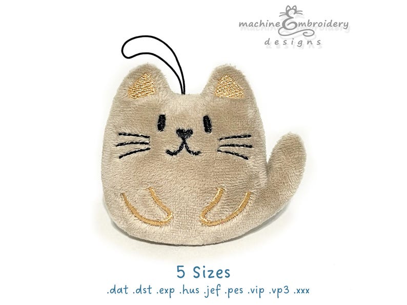 May include: A plush cat-shaped ornament in beige with embroidered details. The cat has black whiskers, eyes, and a nose, with gold accents on the ears and paws. A black loop is attached for hanging. The text "machine embroidery designs" and "5 Sizes" are also visible.