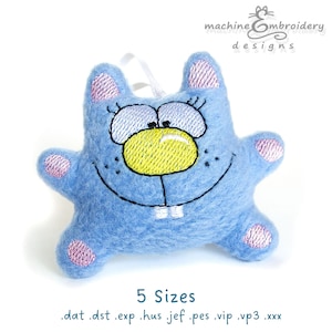 Puede incluir: Juguete de peluche azul con una cara sonriente, nariz amarilla y orejas rosas. El juguete está bordado con una expresión feliz y tiene una boca cosida con dos dientes blancos. El juguete está disponible en 5 tamaños: .dat, .dst, .exp, .hus, .jef, .pes, .vip, .vp3, .xxx.