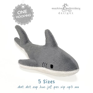 May include: A gray plush shark with a white underbelly, a dorsal fin, and a tail fin. The image includes text that reads "ONE HOOPING", "machine embroidery designs", "5 Sizes", and a list of file formats: .dat .dst .exp .hus .jef .pes .vip .vp3 .xxx.