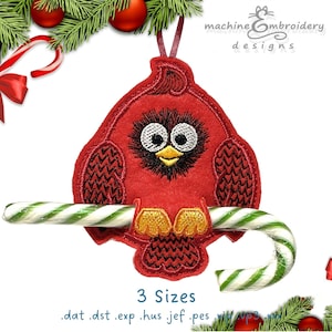 May include: A red cardinal bird ornament with a candy cane. The bird has large eyes and is perched on a green and white striped candy cane. The ornament is surrounded by Christmas decorations, including red ornaments and pine branches.