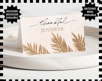 Puede incluir: Una tarjeta de agradecimiento rosa y dorada con un diseño de hojas de palma doradas con purpurina. La tarjeta dice "thankful" en letra cursiva y "JENNIFER" en mayúsculas.