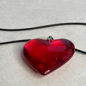 May include: A red glass heart pendant necklace with a black cord.