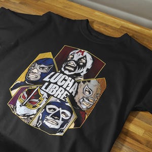 May include: Black t-shirt with a graphic of four masked wrestlers and the words "LUCHA LIBRE" in white. The wrestlers' masks are in blue, red, and white, set against a geometric background. A wrestling-themed garment.