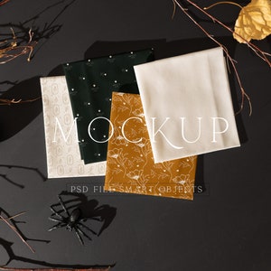 May include: Four fabric swatches with different patterns, including a white background with a small geometric design, a dark green background with a white heart design, a white background with a floral design, and a solid beige fabric. The swatches are arranged on a black surface with branches and a small gourd.