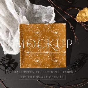 May include: A mockup of a fabric with a white floral pattern on a mustard yellow background. The fabric is surrounded by black branches, white gauze, and black spiders. The text "MOCKUP" is written in white on the fabric. The text "HALLOWEEN COLLECTION | FABRIC" and "PSD FILE SMART OBJECTS" is written in white below the fabric.