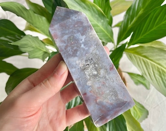 May include: A polished, grey, purple, and white agate crystal point with a natural, rough, and textured surface. The crystal is shaped like a pyramid with a pointed top.