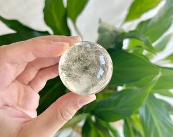 May include: A clear quartz sphere with a cloudy, white, and grey appearance. The sphere is smooth and polished.